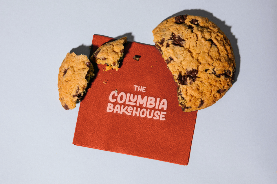 Close-up of a Columbia Bakehouse cookie resting on a napkin printed with the bakery’s logo, designed by Hi Lo Design Co